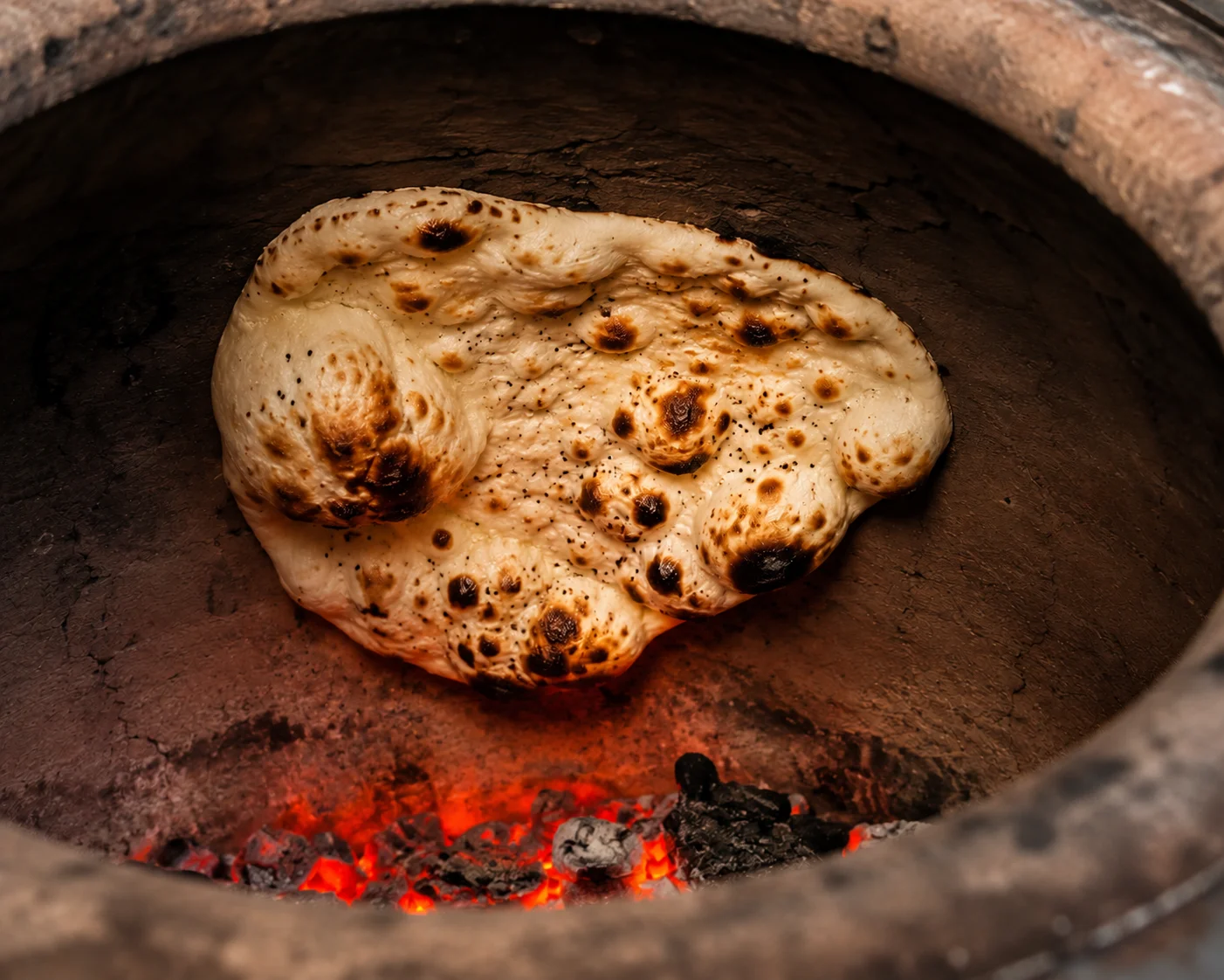 Leavened naan stuck to the wall of a hot clay tandoor, puffing and charring