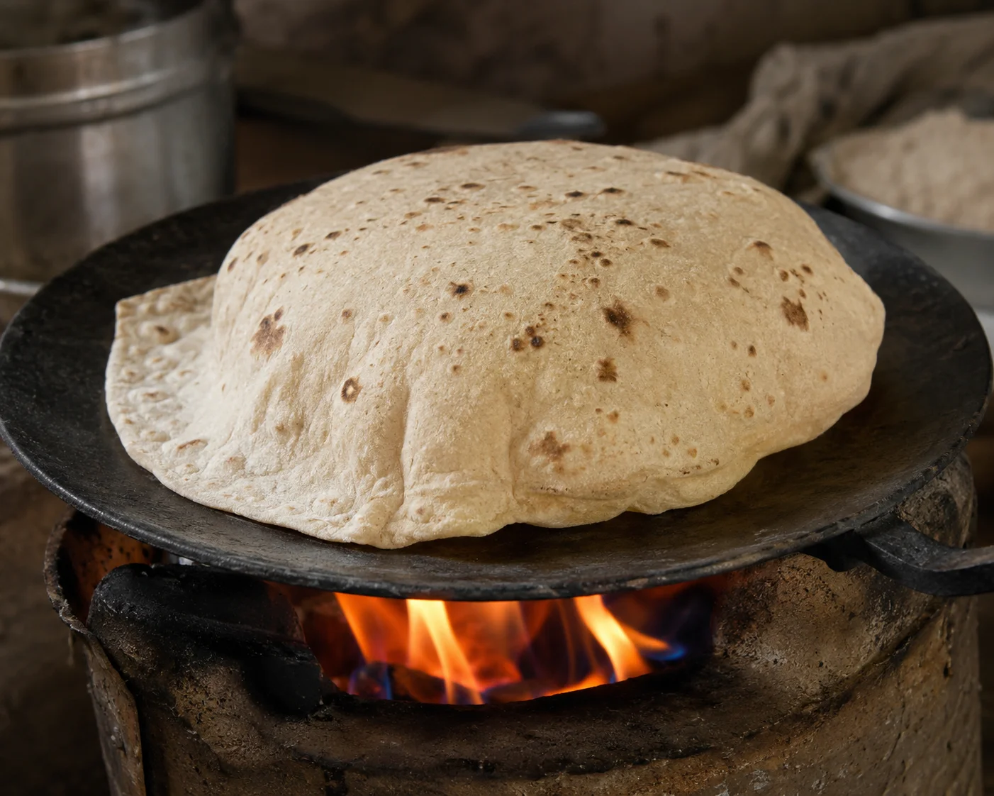 Thin roti puffing up over an open flame on a traditional tawa